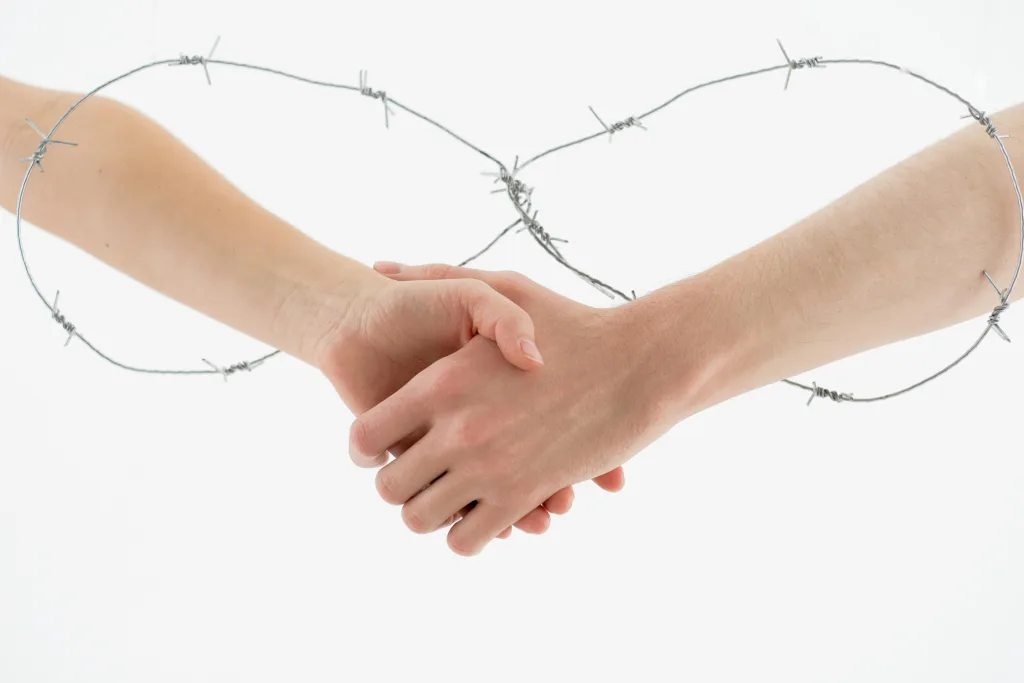 Symbolic handshake wrapped in barbed wire on a white background representing restriction and unity.